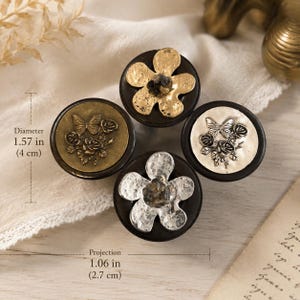 May include: Four circular cabinet knobs with dark wooden bases. Two knobs feature metallic flower shapes with textured centers, while two feature embossed butterfly and rose designs. The knobs have a diameter of 1.57 inches and a projection of 1.06 inches.