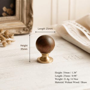 May include: A spherical dark brown walnut wood knob set on a circular brass base. The knob has a height of 35mm or 1.38 inches and a length of 25mm or 0.98 inches. The weight is 21.4 grams or 0.76 ounces. The hardware features a smooth finish.