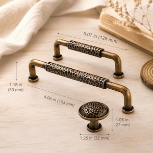 May include: Two antique brass cabinet pulls and one matching round knob with a hammered texture. The pulls measure 5.07 inches and 4.06 inches in length, with a height of 1.18 inches. The round knob measures 1.25 inches wide and 1.06 inches high.