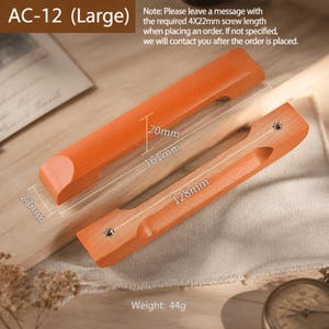 Puede incluir: Dos tiradores de armario de madera marrón claro etiquetados como AC-12 (Large). Los tiradores cuentan con una zona de agarre empotrada. Las anotaciones técnicas indican una longitud total de 161mm, 23mm de ancho, 20mm de alto, 128mm de distancia entre orificios y un peso de 44g.