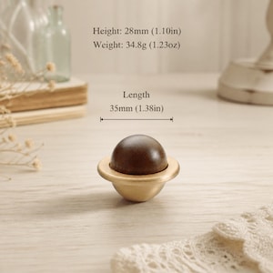 Op de afbeelding: Een meubelknop met een donkerbruine houten bol in een geborstelde messing basis. De knop heeft een hoogte van 28 mm, een gewicht van 34,8 gram en een lengte van 35 mm. Het ontwerp bestaat uit een gladde, ronde houten bovenkant op een metalen voet.