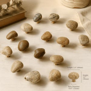 Peut inclure: Une collection de quinze boutons de placard avec des dessus en pierre naturelle dans diverses nuances de brun, gris et beige, chacun monté sur une petite base couleur laiton. Les boutons mesurent 40 mm de long, 30 mm de haut et 12 mm de diamètre.