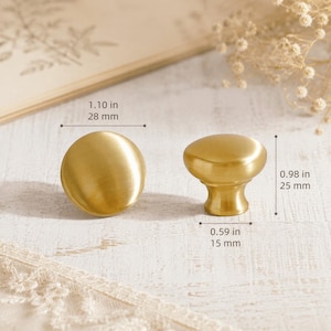 May include: Two round, brushed gold cabinet knobs. One knob is shown from the top, measuring 1.10 inches in diameter. The other knob is shown from the side, measuring 0.98 inches in height and 0.59 inches at the base diameter.