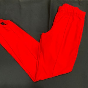 May include: Bright red stirrup pants. These pants feature a high waist with an elastic waistband and stirrups at the ankles. The pants are made of a smooth, solid-colored fabric.