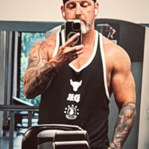 May include: A black tank top with white trim featuring a white bull logo and graphic text on the chest. The garment has a deep scoop neckline and wide shoulder straps, constructed from a lightweight fabric suitable for athletic activity.