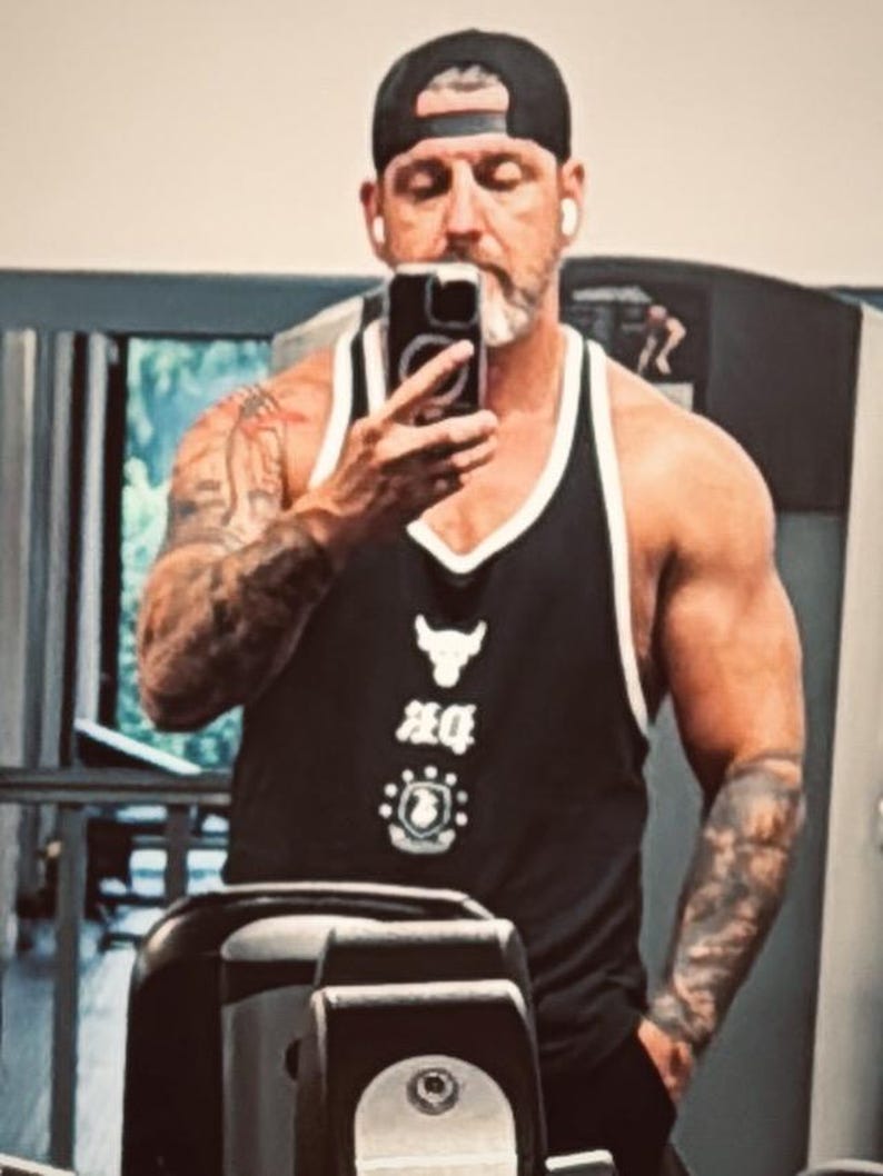 May include: A black tank top with white trim featuring a white bull logo and graphic text on the chest. The garment has a deep scoop neckline and wide shoulder straps, constructed from a lightweight fabric suitable for athletic activity.