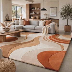 May include: A large rectangular area rug featuring a flowing, abstract wave pattern in shades of cream, beige, and burnt orange. The design consists of layered, curved sections with varying pile heights that create a textured, three-dimensional effect.