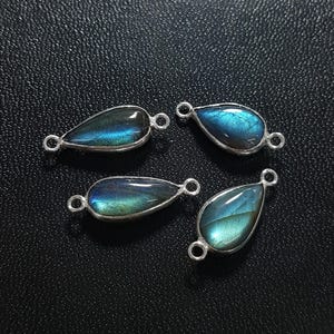 May include: Four teardrop-shaped labradorite gemstones set in silver-toned metal frames. Each stone displays a blue and green iridescent sheen. Every piece features two small circular loops on opposite ends, designed for connecting to jewelry chains.