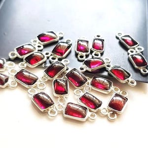 May include: A collection of rectangular silver-toned jewellery connectors, each featuring a deep red, translucent gemstone-like insert. Every piece has two small circular loops on opposite ends, designed for linking components in jewellery assembly.