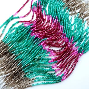 Könnte beinhalten: Mehrere Stränge aus kleinen, facettierten Perlen, die in einem fließenden, wellenförmigen Muster angeordnet sind. Die Perlen weisen einen lebendigen Farbverlauf von leuchtendem Fuchsia und tiefem Magenta bis hin zu Smaragdgrün, Rauchbraun und Weiß auf.