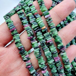 Peut inclure: Une collection de perles de pierres précieuses enfilées sur un cordon, composées de petits morceaux plats et irréguliers de zoïsite verte avec des inclusions magenta vif et noir profond, créant un aspect texturé et multicolore.