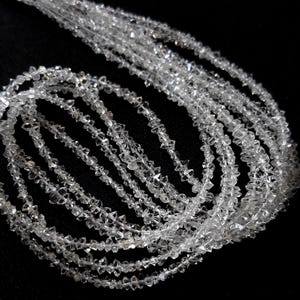 Pode incluir: Um longo fio de cristais de diamante transparentes, brutos e não lapidados. Cada pequena pedra, naturalmente facetada, é incolor, criando uma corrente contínua e cintilante de minerais ásperos e de formas irregulares.