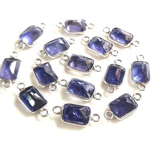 Può includere: Una collezione di connettori rettangolari in vetro sfaccettato viola incastonati in cornici di metallo color argento. Ogni pezzo presenta due piccoli anelli circolari alle estremità opposte, progettati per collegare componenti di gioielleria.