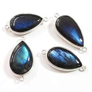 May include: Four teardrop-shaped labradorite gemstones set in silver-toned metal bezels. Each pendant features a smooth, polished surface with iridescent blue flashes and includes two small circular loops at opposite ends for attachment.