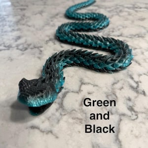 Op de afbeelding: Een flexibel, gearticuleerd slangenfiguur met een kleurverloop van zwart en groenblauw. De slang heeft een gestructureerd, schubachtig oppervlak en is in een gebogen vorm geplaatst. De tekst Green and Black staat op de afbeelding.