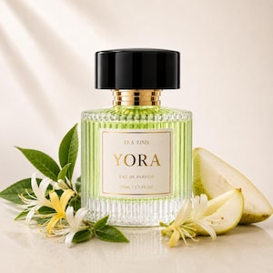 May include: A clear, ribbed glass perfume bottle with a black cap and gold collar. The label reads TEA TIME YORA EAU DE PARFUM 50ML | 1.7 FL.OZ. The bottle is surrounded by white and yellow honeysuckle flowers and slices of a green pear.