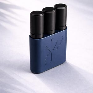 Puede incluir: Un soporte rectangular azul oscuro con bordes redondeados que contiene tres recipientes cilíndricos negros. La parte frontal del soporte azul presenta una letra Y en relieve y una línea curva de pequeñas hendiduras circulares.