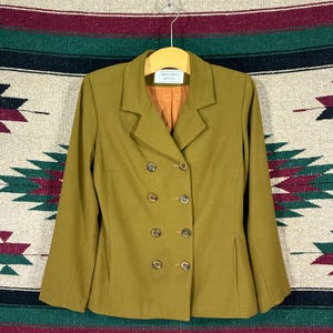 May include: A double-breasted olive green blazer featuring a notched lapel, long sleeves, and eight brown buttons arranged in two vertical rows. The interior lining is a solid orange colour, and a white label reads Beechers Brook.