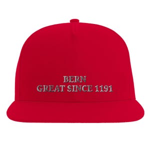 Könnte beinhalten: Eine leuchtend rote Baseballkappe mit flachem Schirm und strukturierter Krone. Auf der Vorderseite befindet sich ein gestickter Schriftzug in einer dunkelgrauen, abgenutzten Schriftart, der "BERN" oben und "GREAT SINCE 1191" unten zeigt.