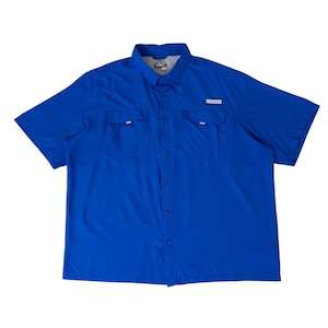 May include: A short-sleeved button-down shirt in a solid royal blue color. The shirt features a pointed collar, a full-length front button placket, and two chest pockets with flaps. A small white rectangular logo patch is visible on the left pocket.