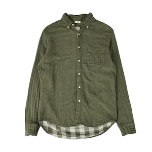 May include: An olive green long-sleeve button-down shirt featuring a button-down collar, a single chest pocket, and a white and olive green checkered pattern on the interior hem. The shirt is constructed with a textured fabric and light buttons.