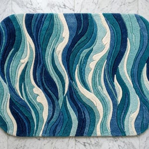 Op de afbeelding: Een rechthoekig tapijt met afgeronde hoeken voorzien van een getextureerd, getuft patroon van verticale, golvende lijnen in diverse tinten diep marineblauw, talingblauw, lichtblauw en crème, wat zorgt voor een gelaagde, driedimensionale uitstraling.
