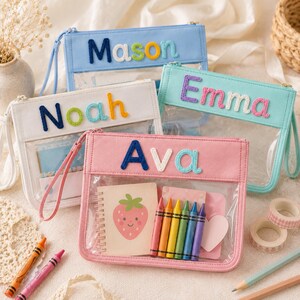 Puede incluir: Cuatro estuches rectangulares con cremallera, frente de vinilo transparente y bordes de tela en azul claro, blanco, turquesa y rosa. Cada estuche presenta un nombre personalizado con letras de tela coloridas y texturizadas.