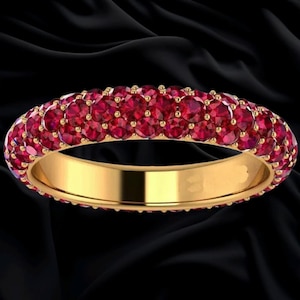 May include: A gold band ring featuring three rows of small, round, vibrant red gemstones set closely together across the entire outer surface of the metal band, creating a continuous pavé style design with a polished yellow gold interior.