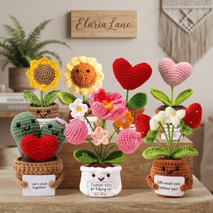 May include: A collection of six crocheted potted plants featuring various designs including sunflowers, hearts, and cacti. Each pot has a smiling face and holds a small white sign with text such as Let's stick together, Thank you for helping me grow, and Life would succ without you.