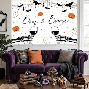 May include: A rectangular wall art print featuring a white background with the black text Boos & Booze. The design includes black skeleton hands holding wine glasses, orange pumpkins, black bats, spider webs, and small white ghost illustrations.