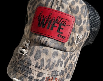 May include: A brown and black leopard print trucker hat with a red patch that says "firefighter wife" in black lettering. The patch also has the number "6542" in black lettering.