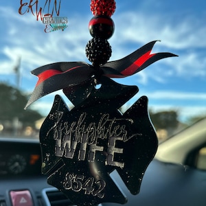 May include: Black and red firefighter wife car charm with a black and red ribbon and a black and red beaded chain. The charm is shaped like a firefighter's Maltese cross with the words "firefighter wife" and the number "8542" inscribed on it.