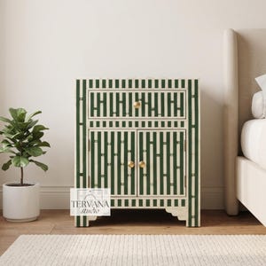 May include: A rectangular bedside table featuring a green and white striped pattern with a bone inlay finish. The piece includes one top drawer and two lower cabinet doors, each accented with small, round, gold-toned metal knobs.