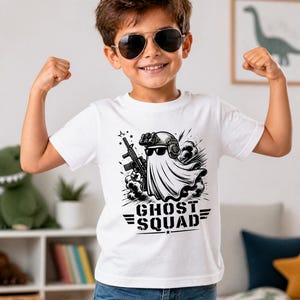 May include: A white short-sleeved t-shirt featuring a black and white graphic of a ghost wearing a tactical helmet and sunglasses while holding a rifle. Below the ghost, the text GHOST SQUAD is printed in a bold, stencil-style font with wings.