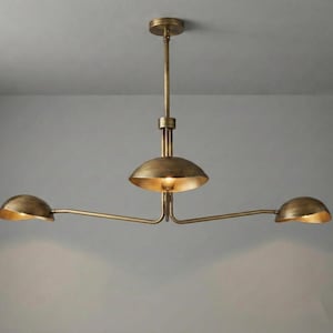 May include: A brass chandelier featuring a central vertical rod connected to three horizontal arms. Each arm terminates in a shallow, bowl-shaped shade facing downward, with a warm light emitting from the center of each metallic dome fixture.