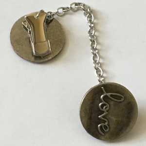 May include: Silver tone love charm with a clip on the back and a chain connecting to a round charm with the word "love" engraved on it.