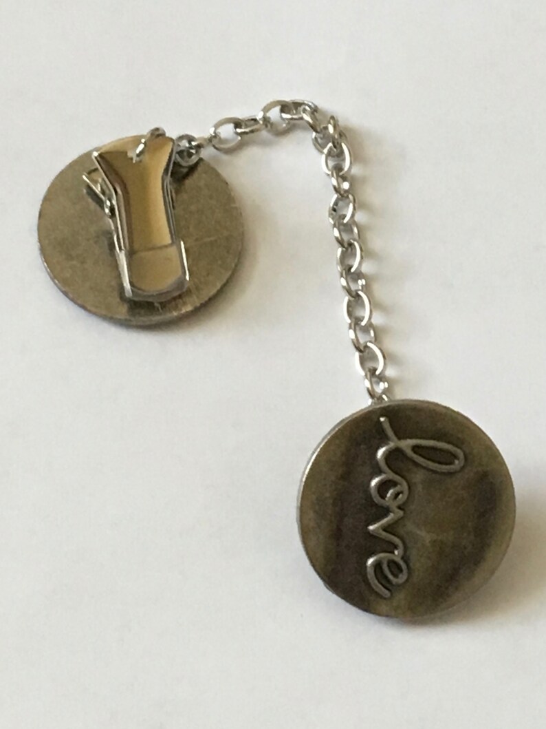 May include: Silver tone love charm with a clip on the back and a chain connecting to a round charm with the word "love" engraved on it.