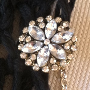 May include: A silver flower-shaped brooch with clear rhinestones. The brooch is attached to a silver chain.