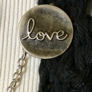 May include: A silver charm with the word "love" inscribed on it. The charm is attached to a silver chain.