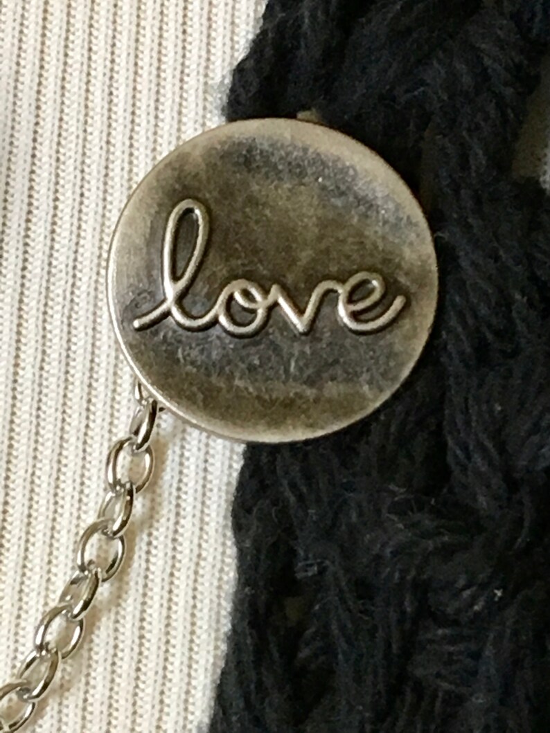 May include: A silver charm with the word "love" inscribed on it. The charm is attached to a silver chain.