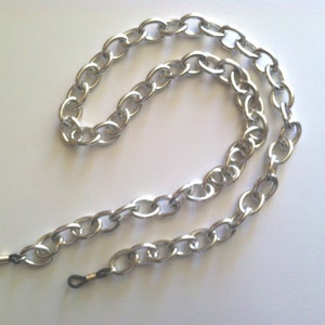 May include: Silver chain eyeglasses holder with black rubber earpieces. The chain is made of linked oval shapes.