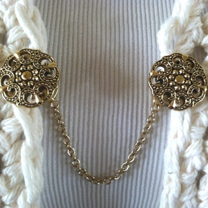 The mattie gold tone resin medallion sweater clip adds a touch of vintage elegance to your wardrobe.