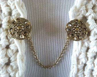 The mattie gold tone resin medallion sweater clip adds a touch of vintage elegance to your wardrobe.
