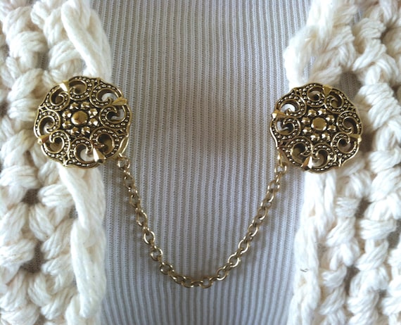 The mattie gold tone resin medallion sweater clip adds a touch of vintage elegance to your wardrobe. 