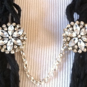 May include: A pair of silver chain scarf clips with clear rhinestone flower accents.