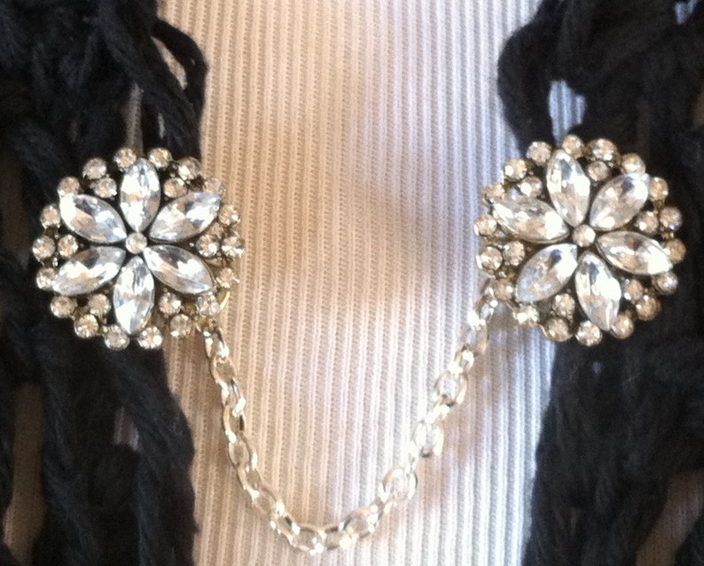 May include: A pair of silver chain scarf clips with clear rhinestone flower accents.
