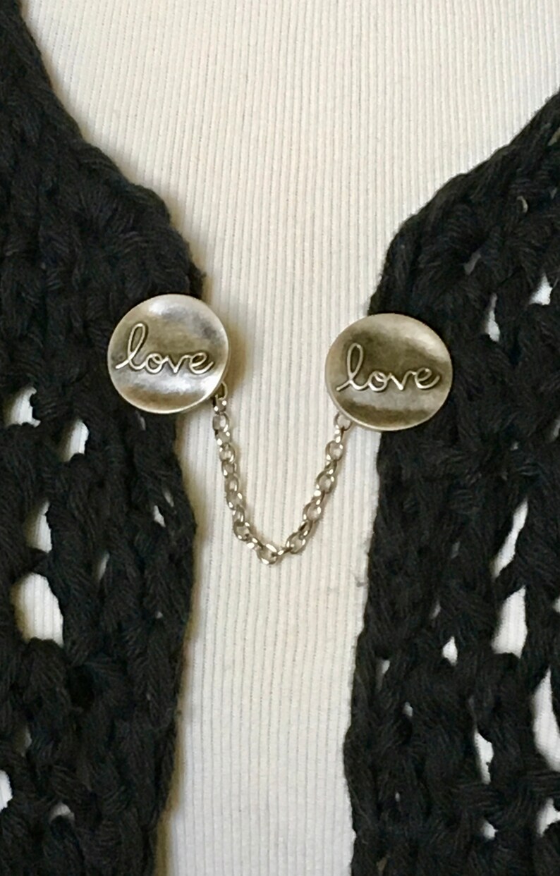 May include: A pair of silver tone metal clasps with a chain connecting them. Each clasp has the word "love" engraved on it.
