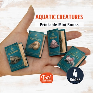 May include: Four miniature printable books titled Aquatic Creatures, featuring illustrations of a mudskipper, nautilus, blobfish, and axolotl on teal covers with gold text and crowns. Each small book has visible paper pages and a classic design.