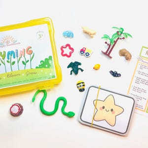 May include: A yellow plastic storage case labeled Simply Sunbloom Rhyming Learn Bloom Grow, containing various small plastic animal and object figurines, a green snake, a deck of star-illustrated cards, and a Rhyming Sounds instructional sheet.