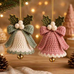 May include: Two crocheted bell ornaments hanging by gold strings. One bell is cream with a sage green bow, the other is dusty pink with a matching bow. Both feature dark green crocheted holly leaves, three small cream berries, and a gold jingle bell.